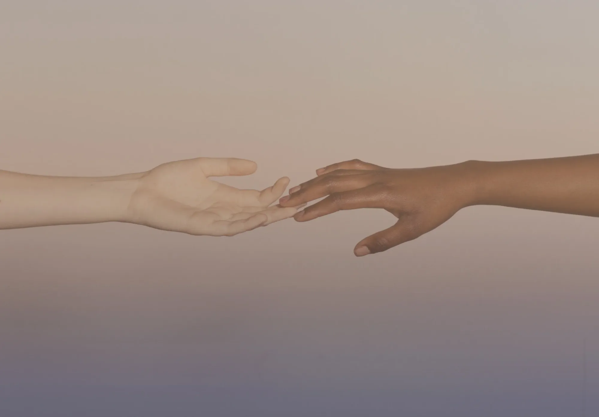 Two hands reaching toward each other against a soft, hazy sky