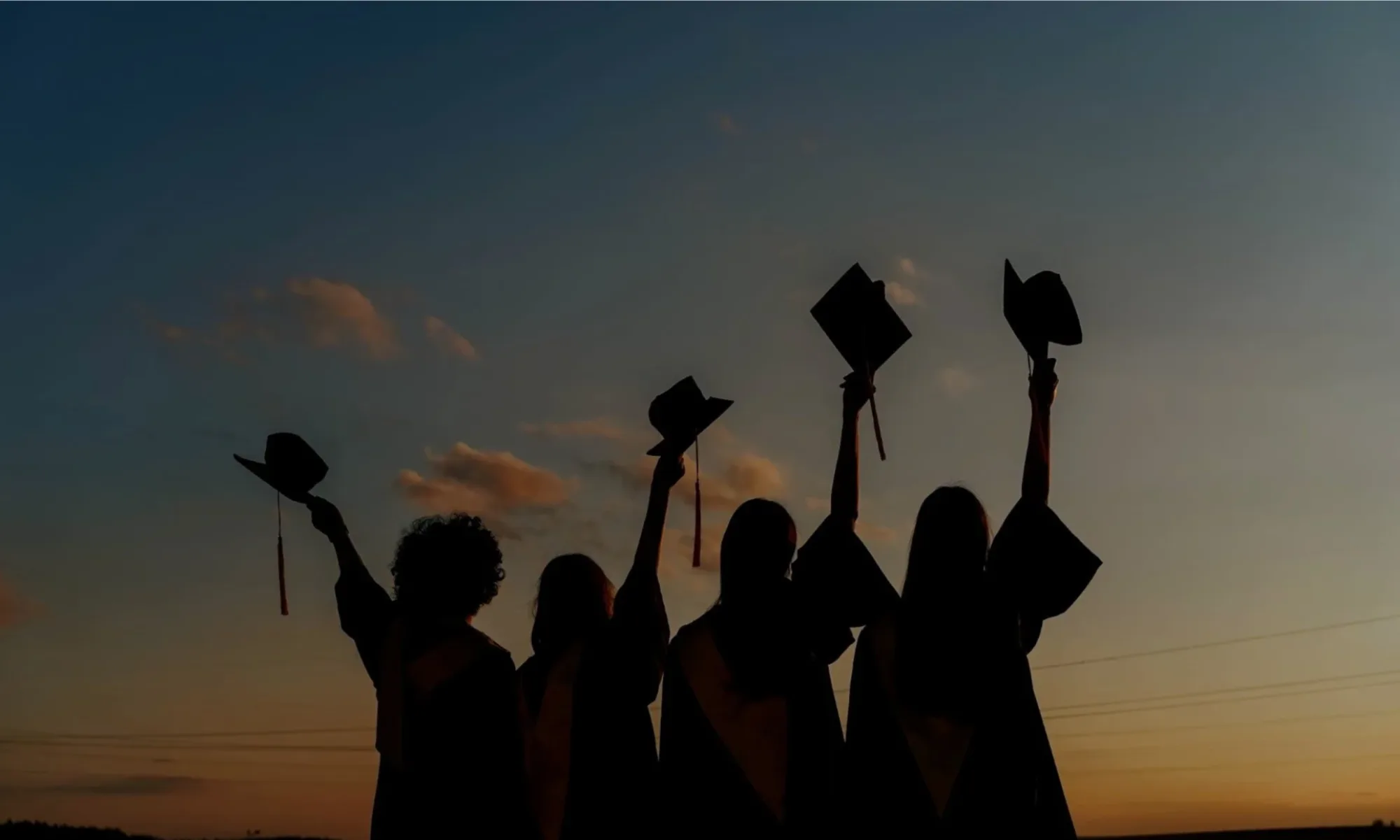 Graduates silhouetted against a sunset, caps raised in celebration