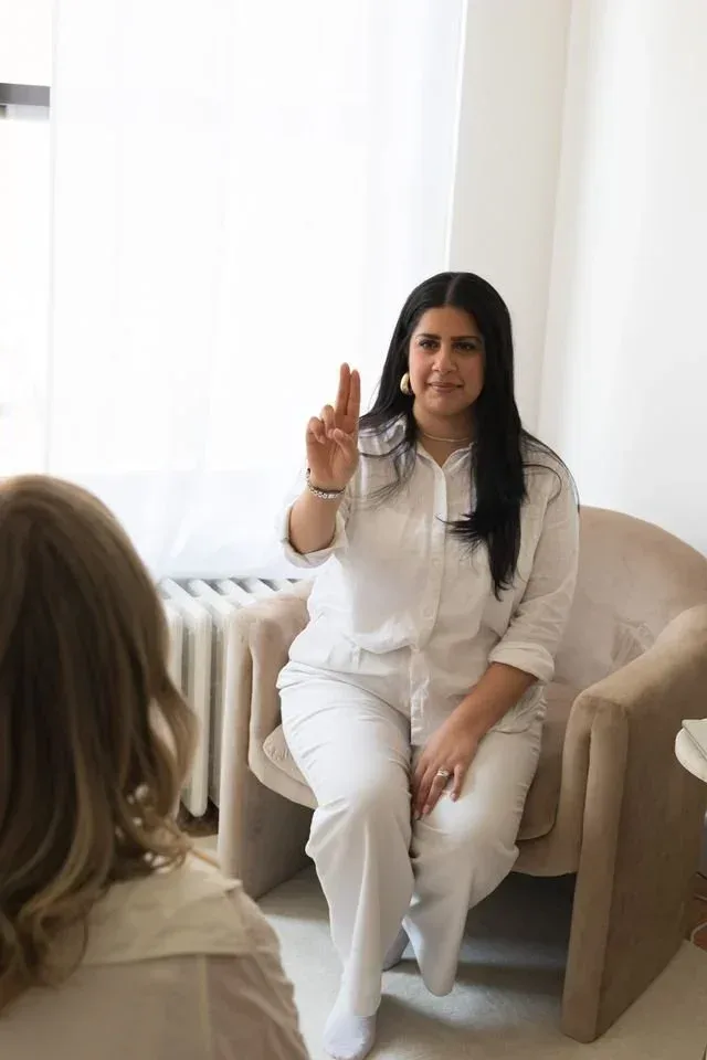 Woman in white seated in an armchair, gesturing as she speaks