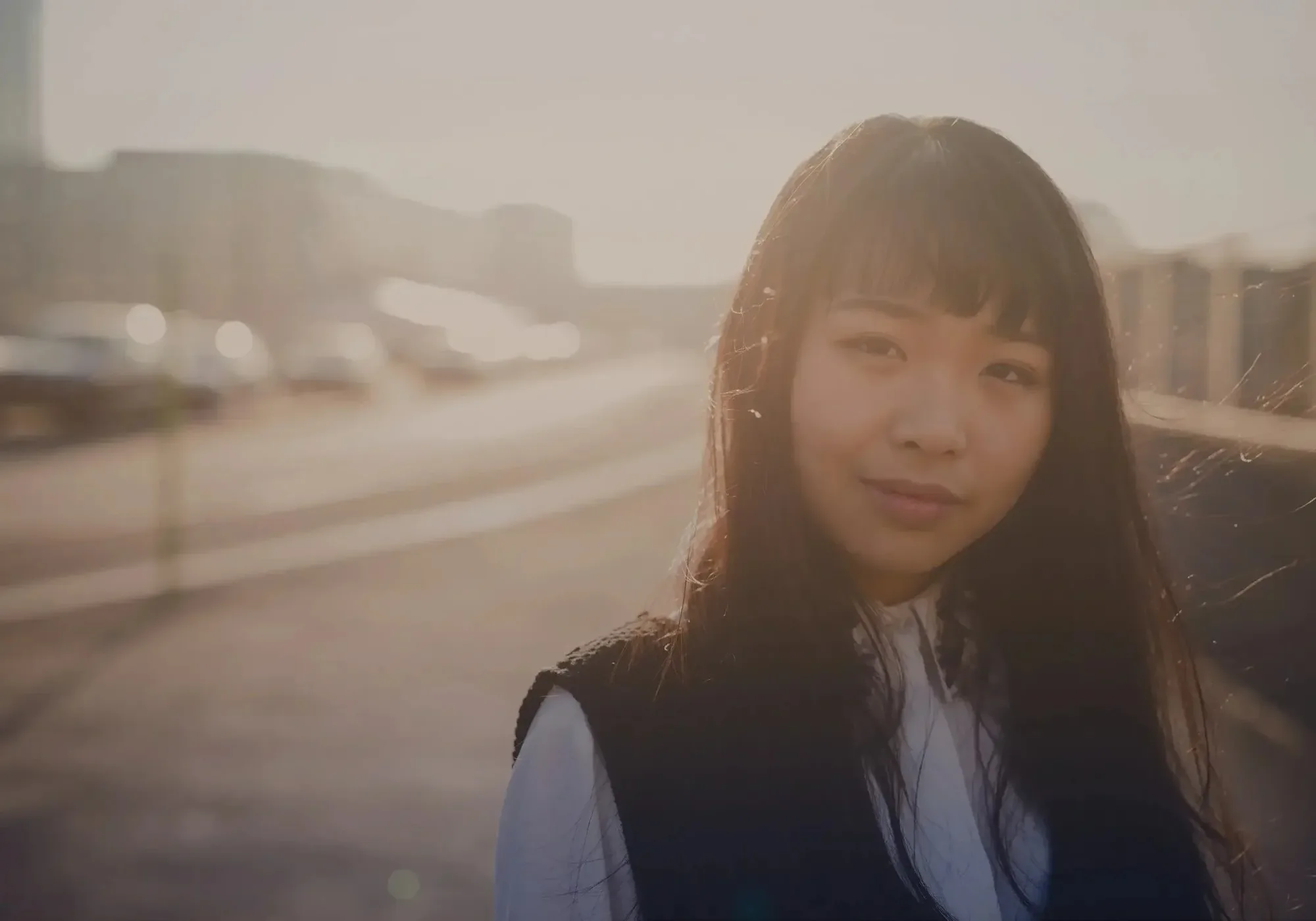 Young East Asian woman looking over her shoulder on a city street at dusk