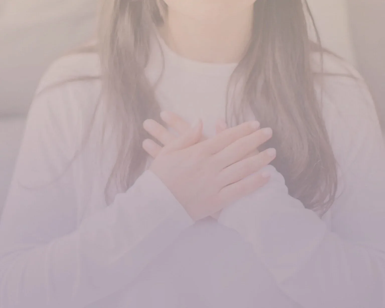 Woman with hands resting on her chest in soft, pale light