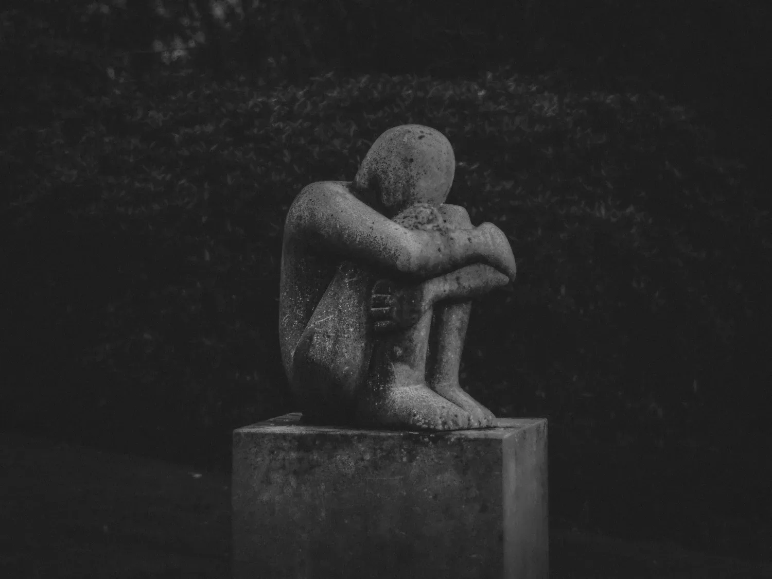 Black-and-white photo of a stone statue of a figure hugging its knees