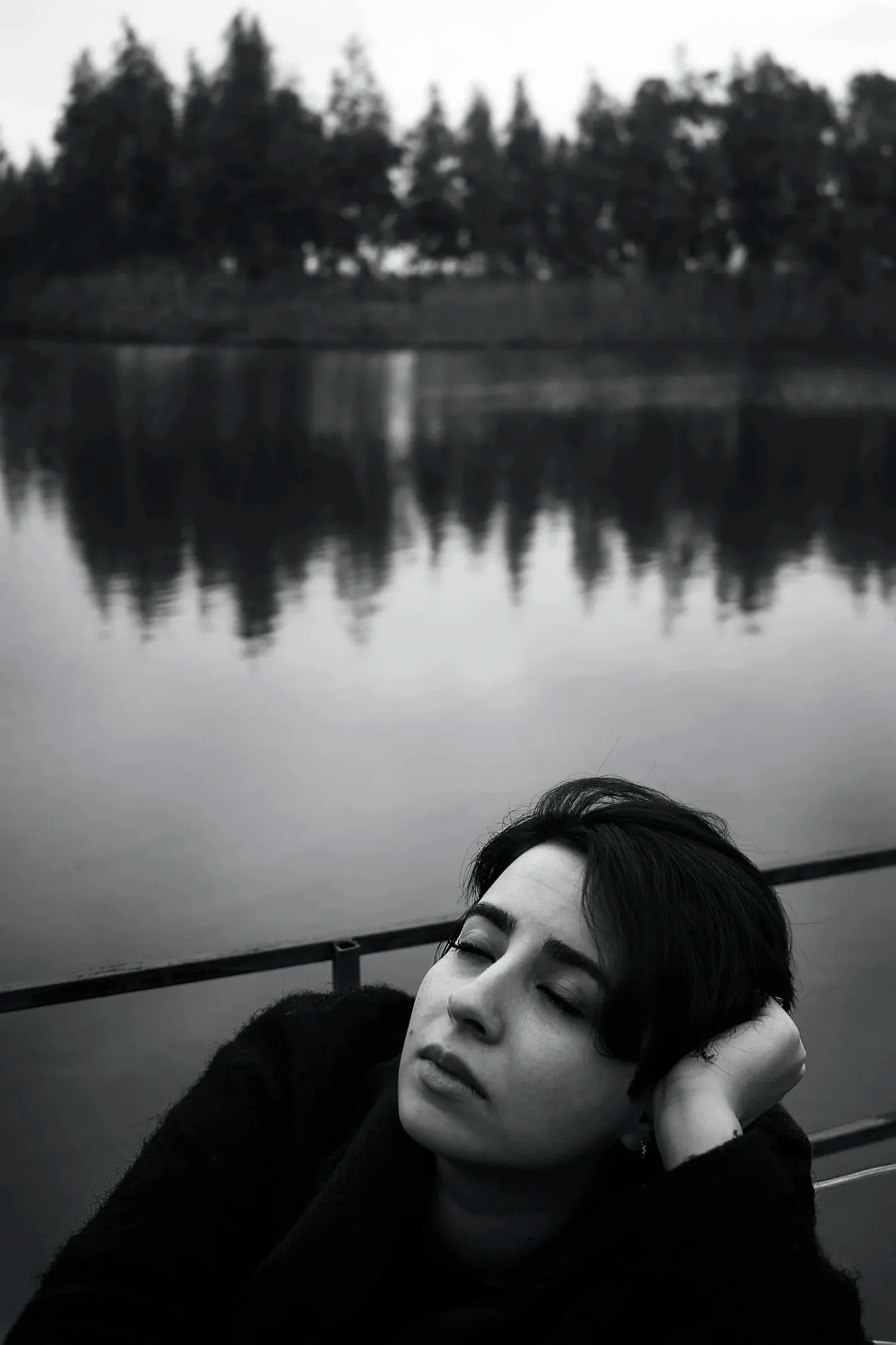 Black-and-white photo of a person resting their head beside a still lake