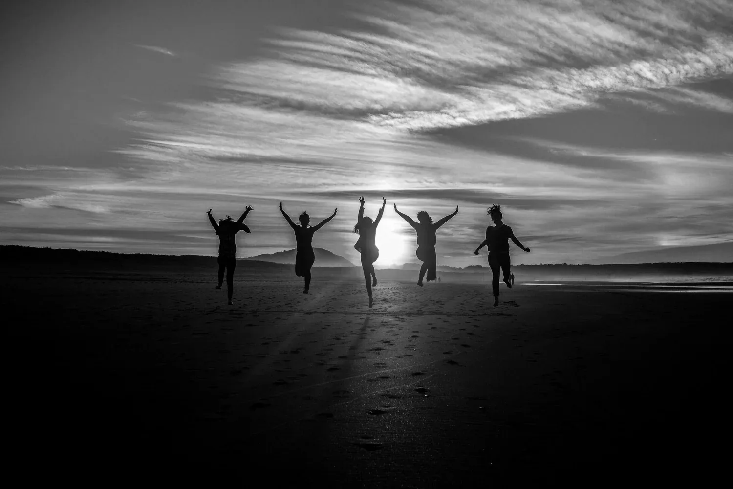 Black-and-white silhouettes of friends jumping on a beach at sunset