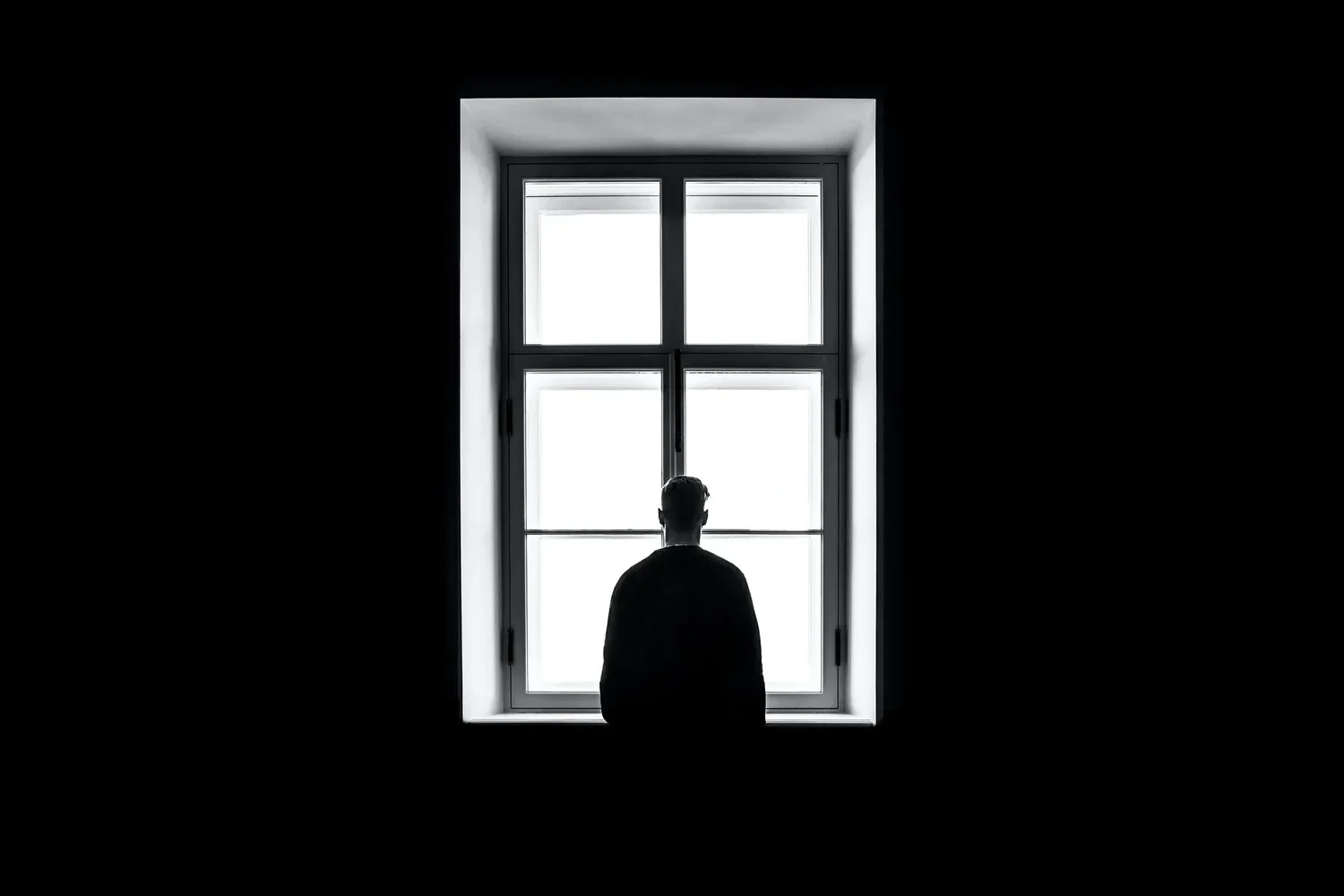 Silhouette of a person standing in front of a bright window in a dark room