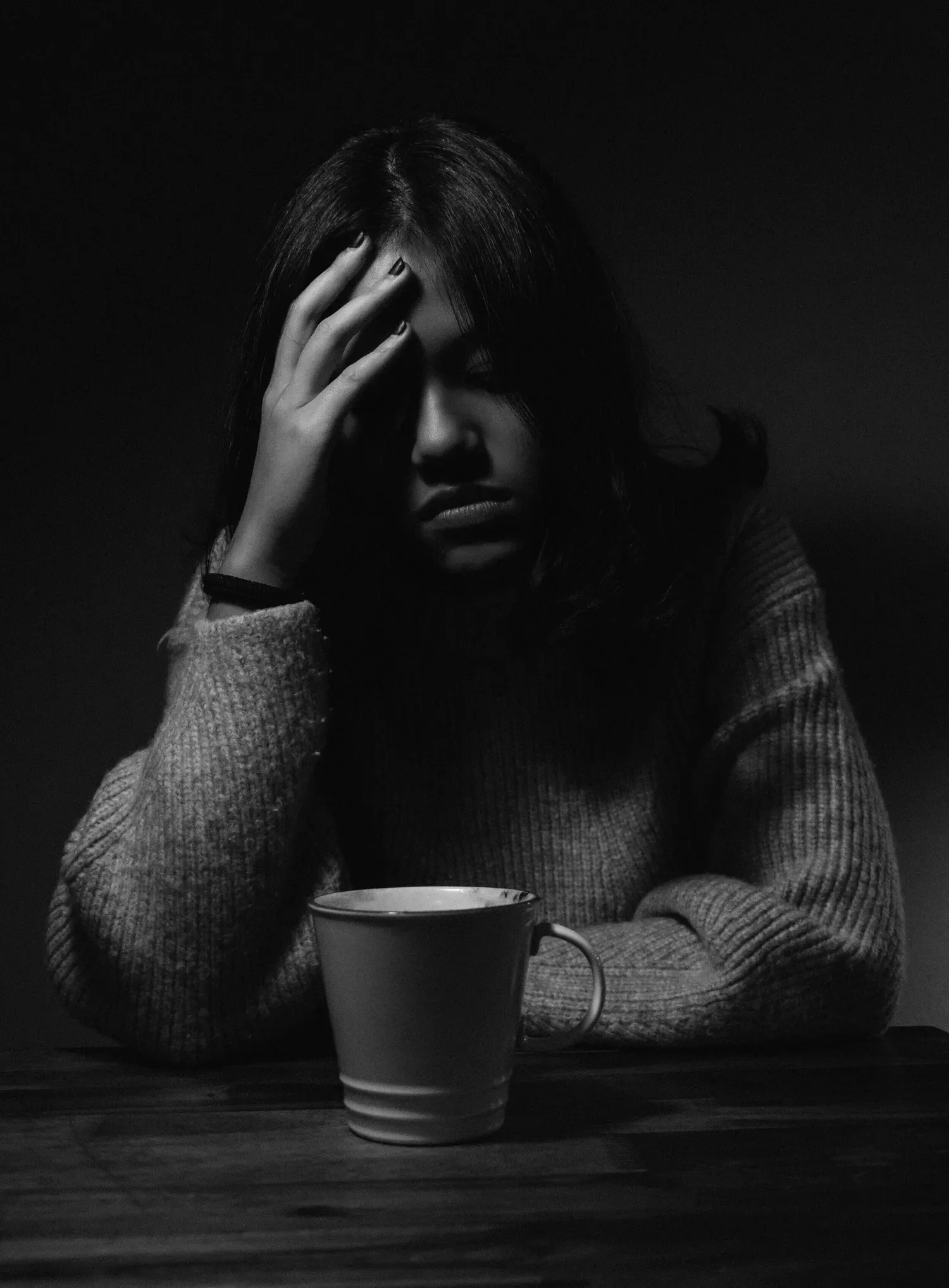 Black-and-white photo of a person with a hand to their forehead beside a mug