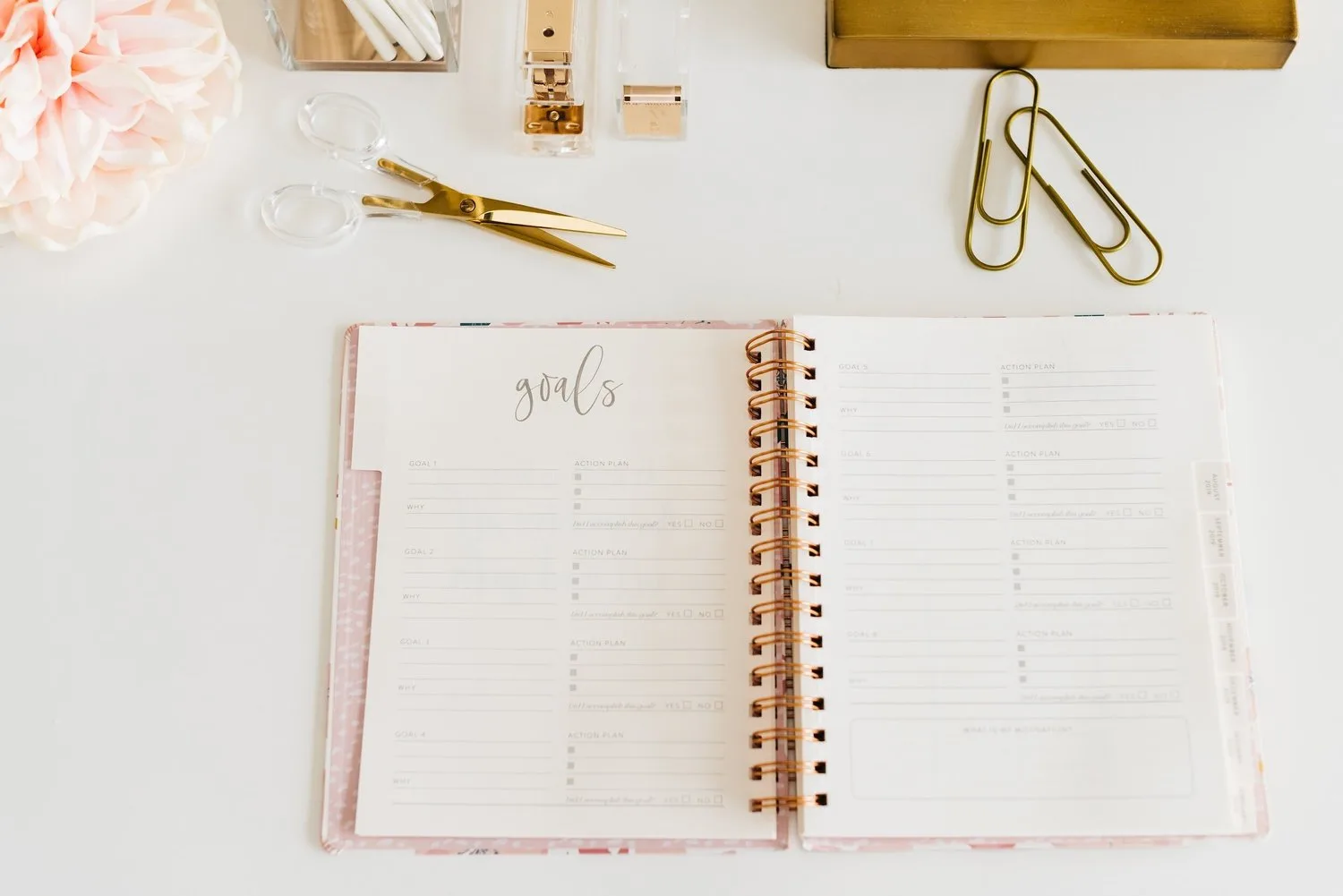 Open planner on a white desk with gold paper clips and flowers