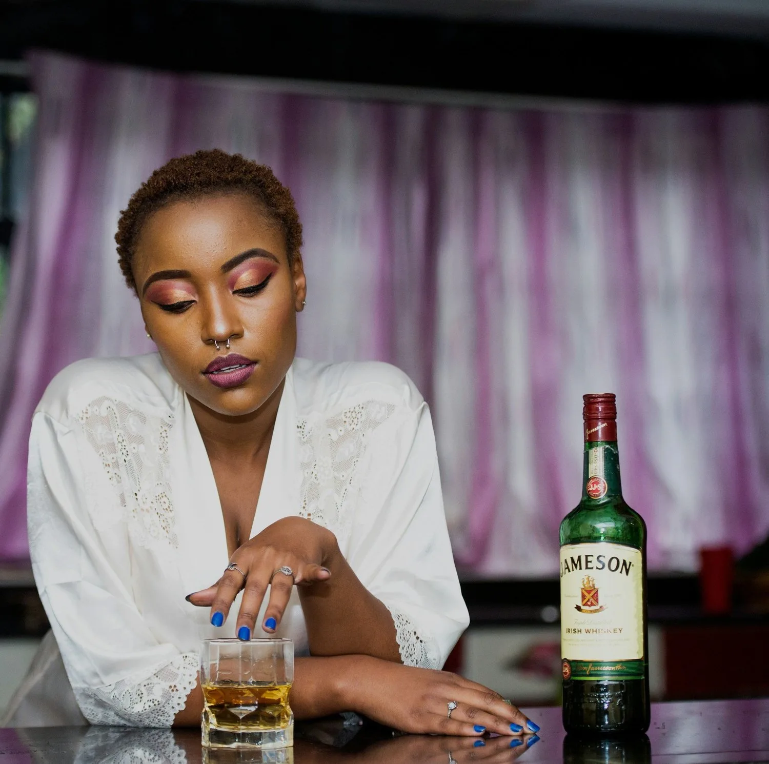 Woman at a table looking down at a glass beside a whiskey bottle