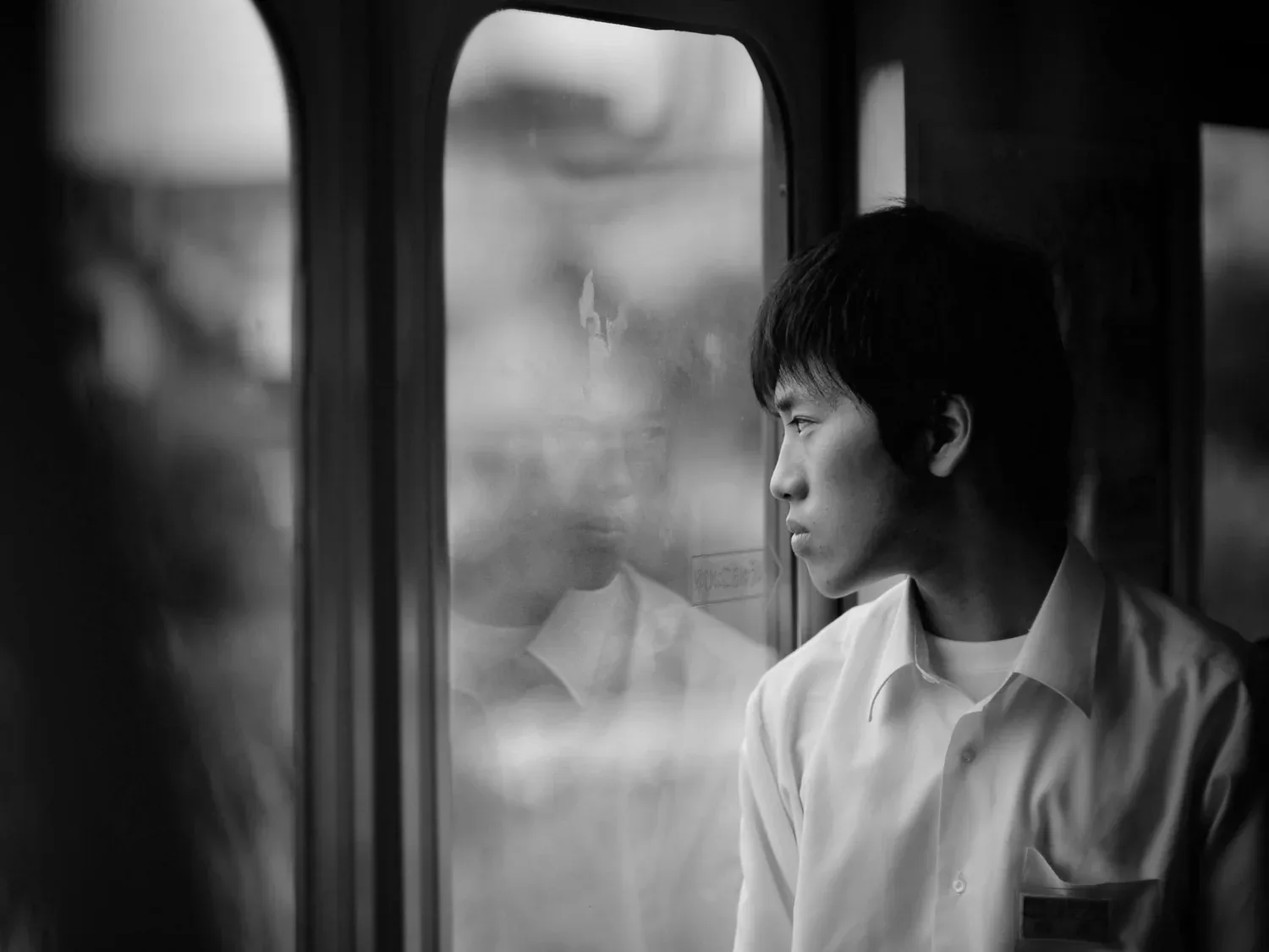 Black-and-white photo of a young man looking out a train window