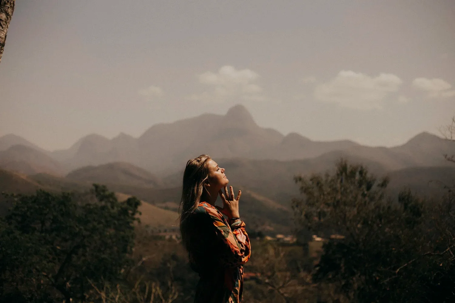 Person standing in tall grass facing distant mountains at dusk