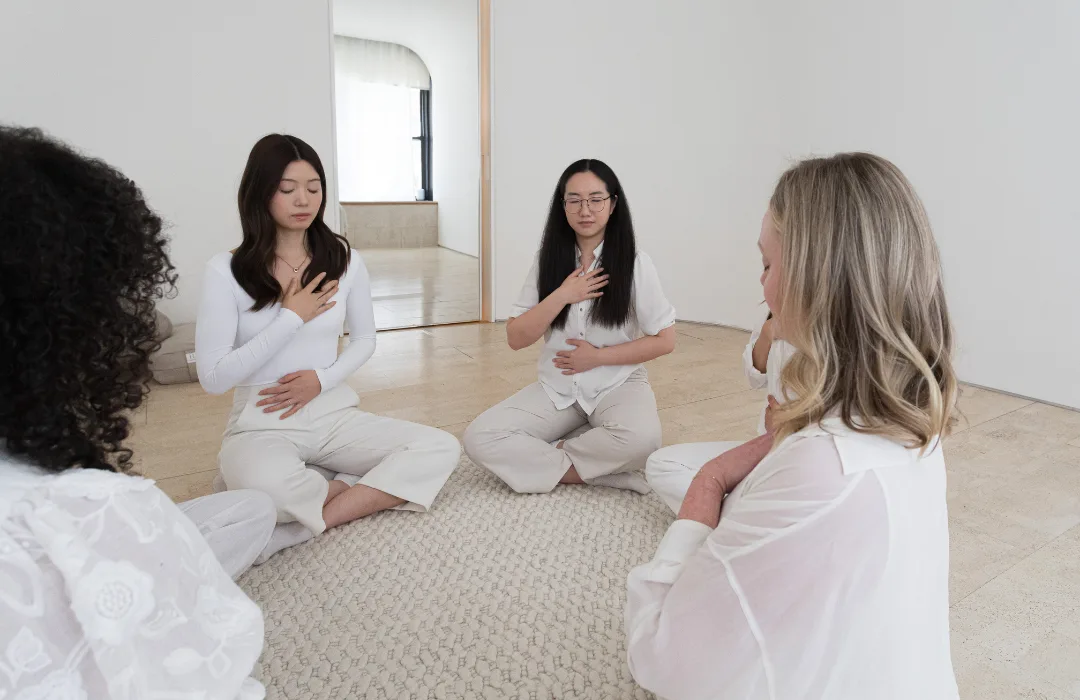Women in white sitting on the floor in a circle during a group session