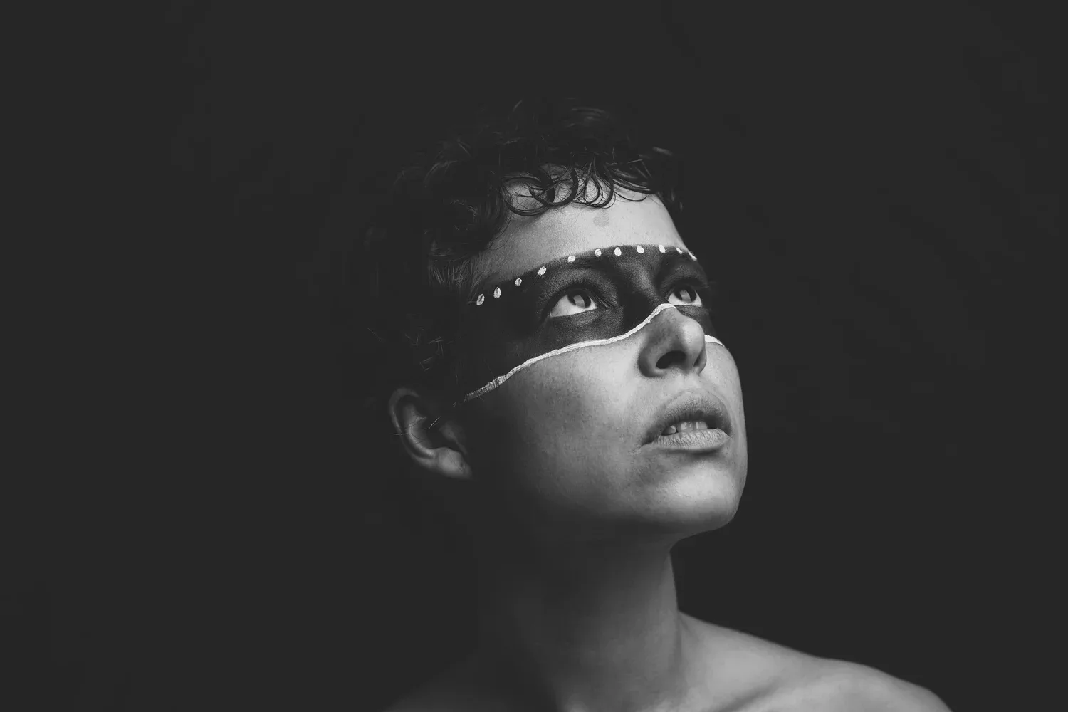 Black-and-white photo of a person with a lace mask looking upward
