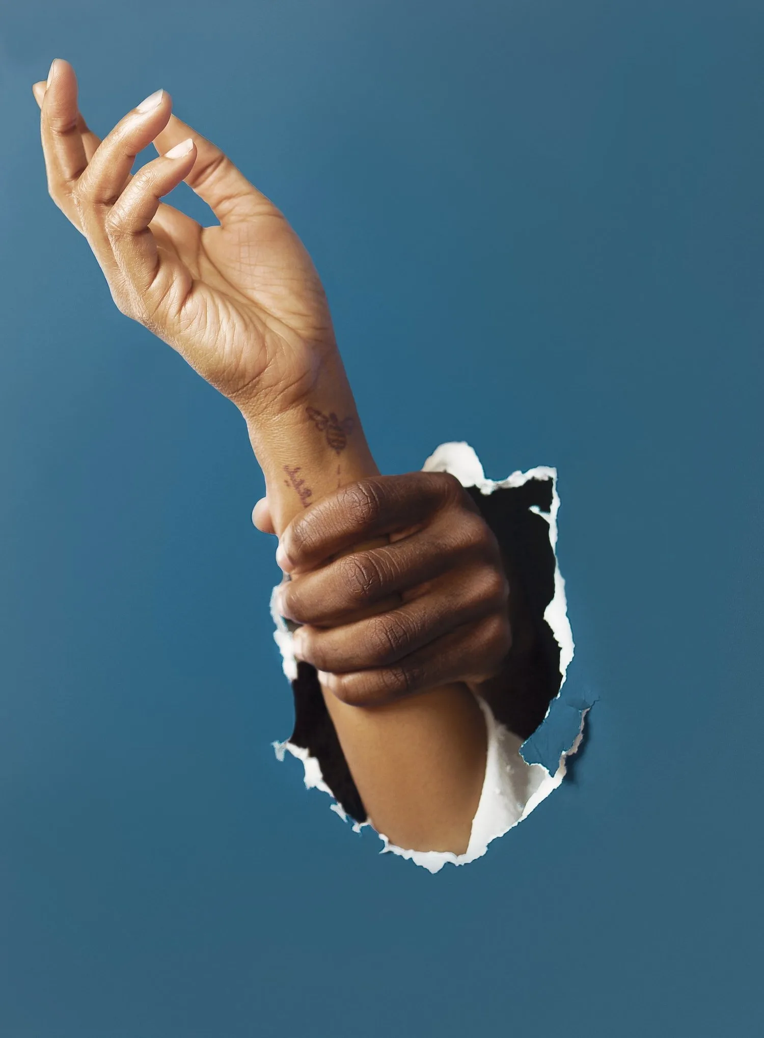 Hand reaching through a torn blue paper background to grasp another hand