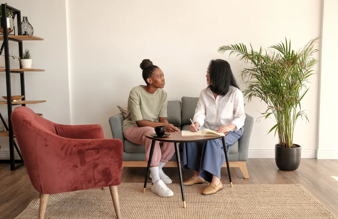 Two women talking on a sofa in a plant-filled therapy office