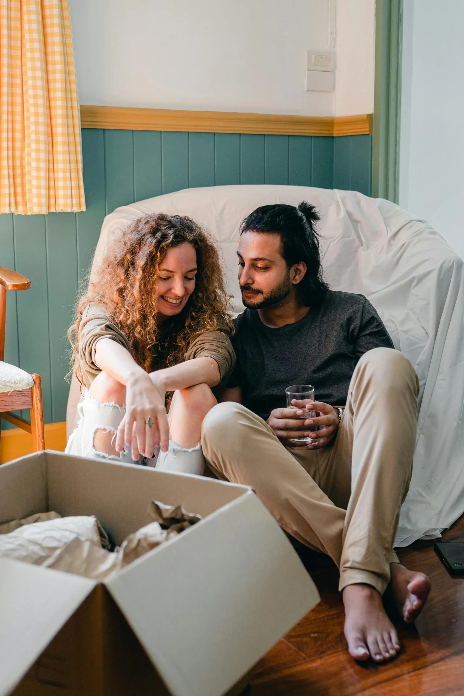 Couple sitting close on the floor beside moving boxes, smiling together