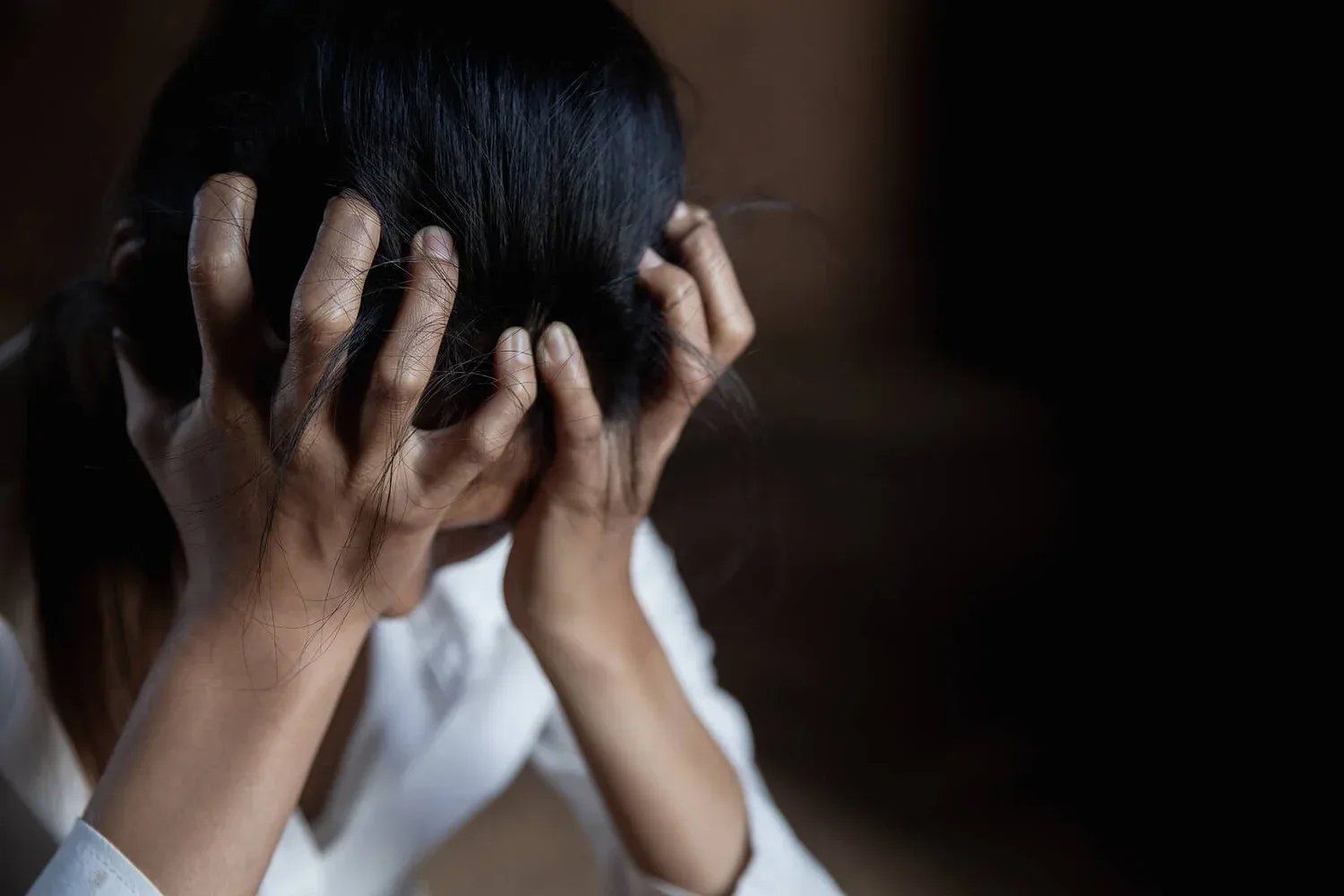 Person holding their head in both hands in dim light