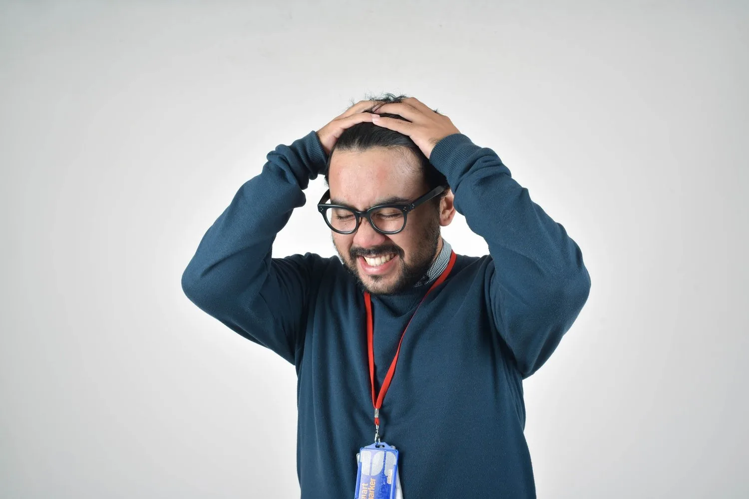 Man in glasses holding his head with both hands, grimacing