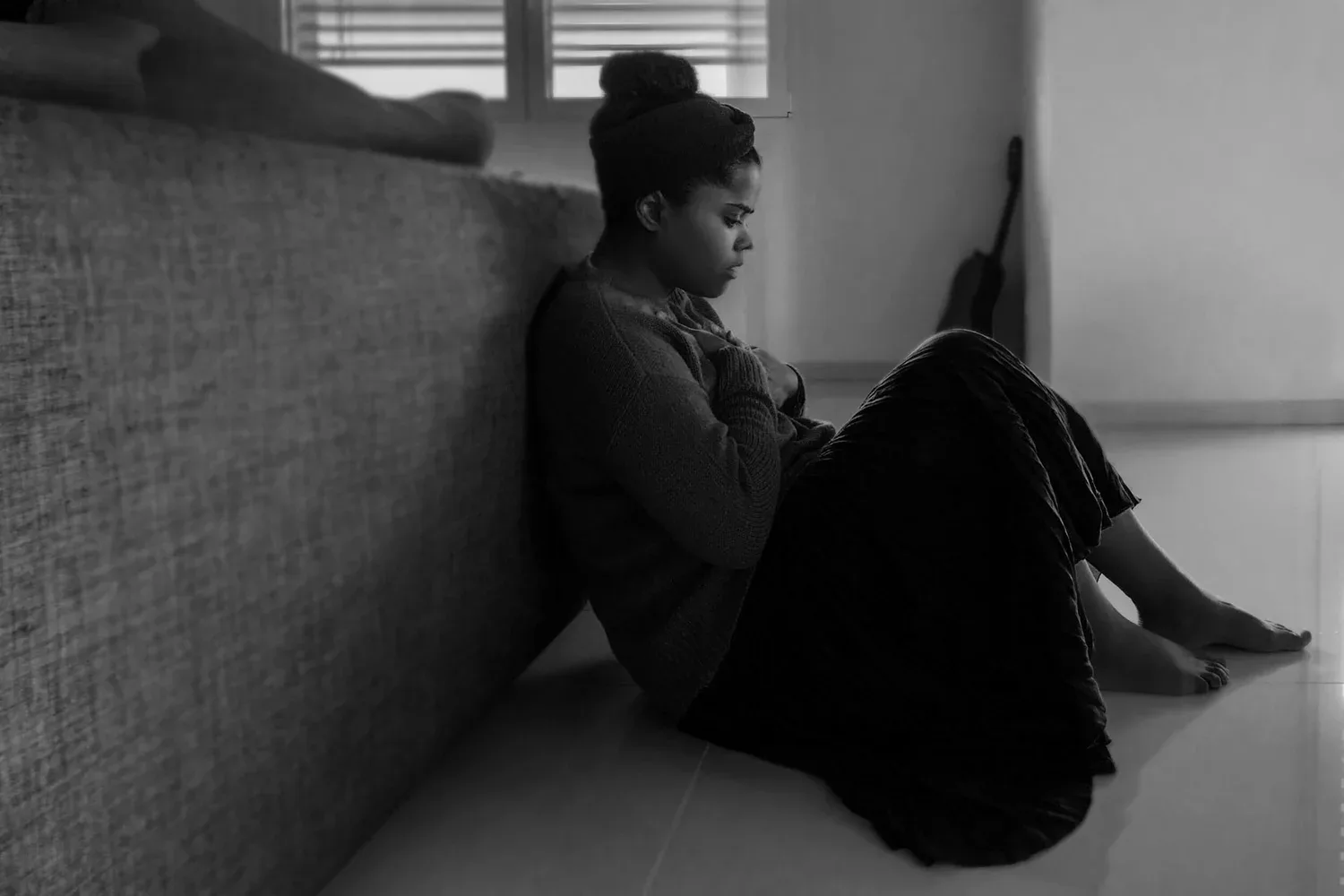 Black-and-white photo of a person sitting on a window seat against a wall