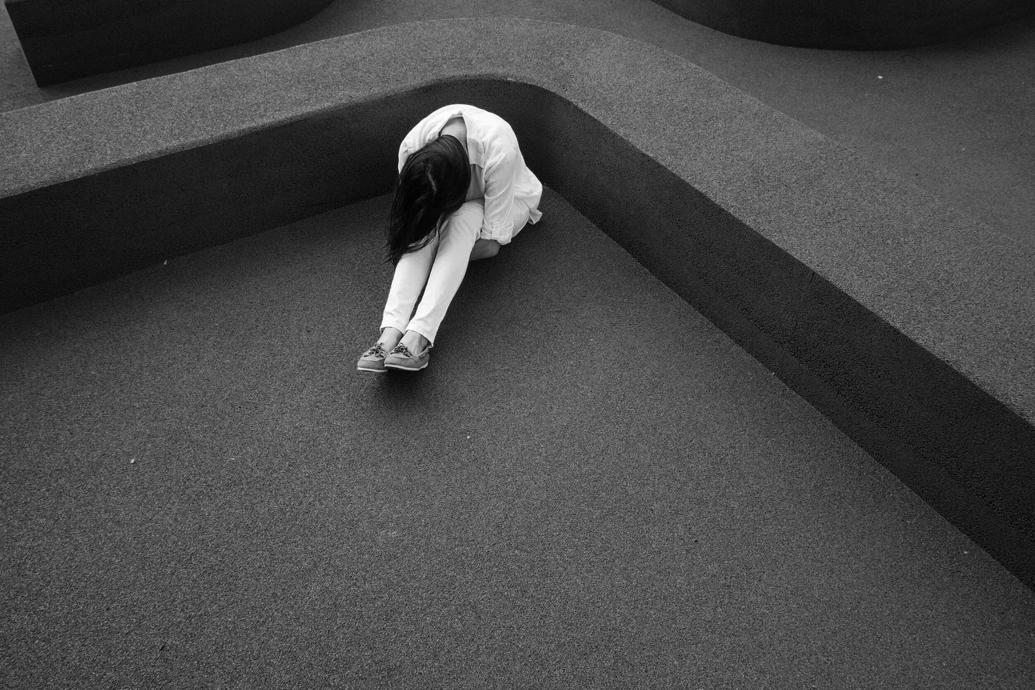 Black-and-white photo of a person curled up alone on a concrete floor
