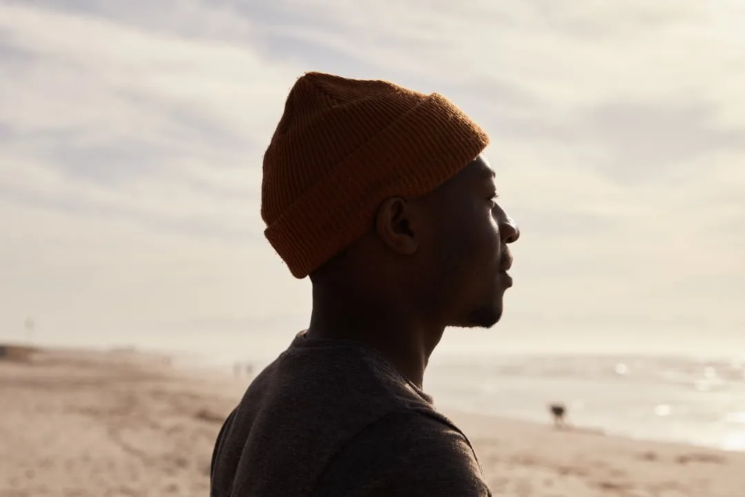 Man in a beanie gazing out toward the ocean at dusk
