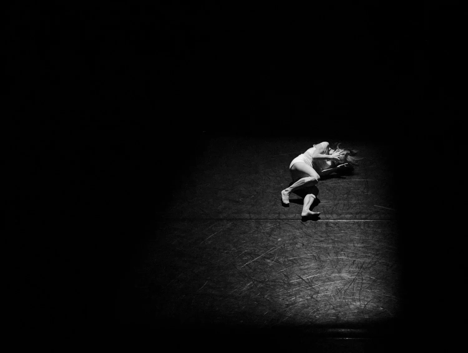 Person curled up alone in a small pool of light in darkness