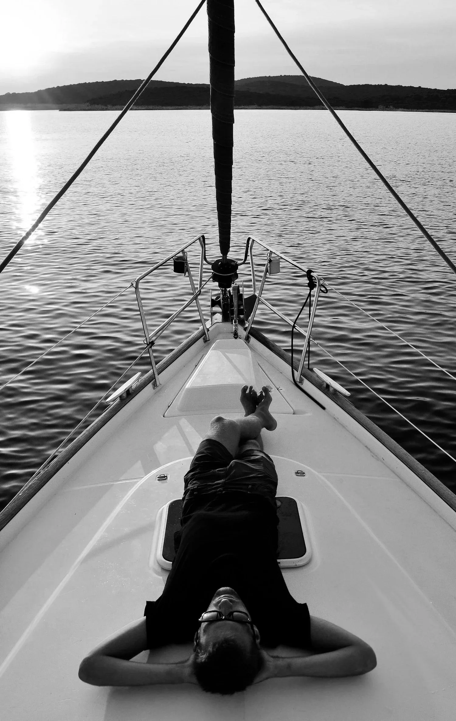 Person lying on the bow of a boat on open water, seen from above