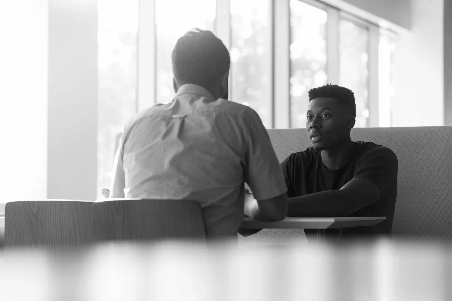 Two men talking across a table in a sunlit room