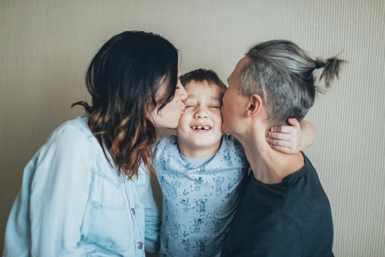 Two mothers kissing their smiling young son on both cheeks