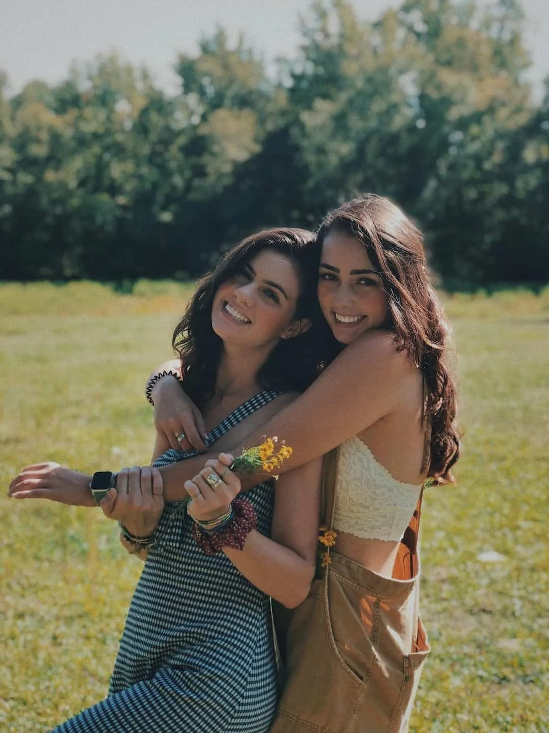 Two women hugging and smiling outdoors in a sunny field