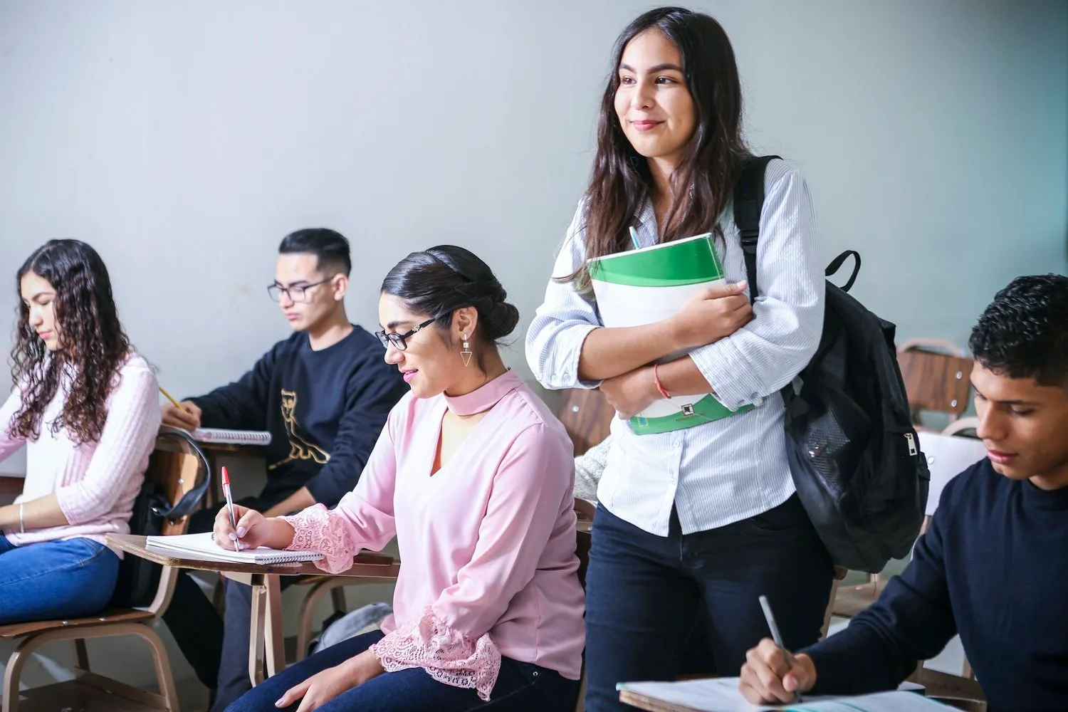 High school students in a classroom, one holding books and smiling