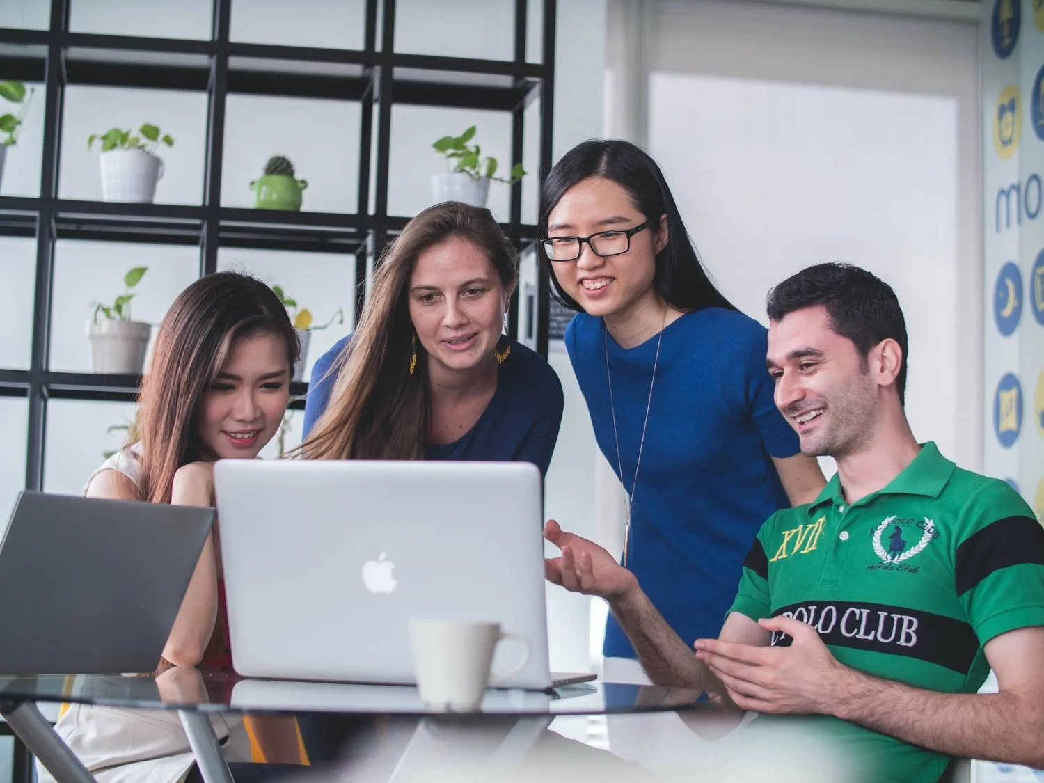 Four young coworkers smiling around a laptop in an office