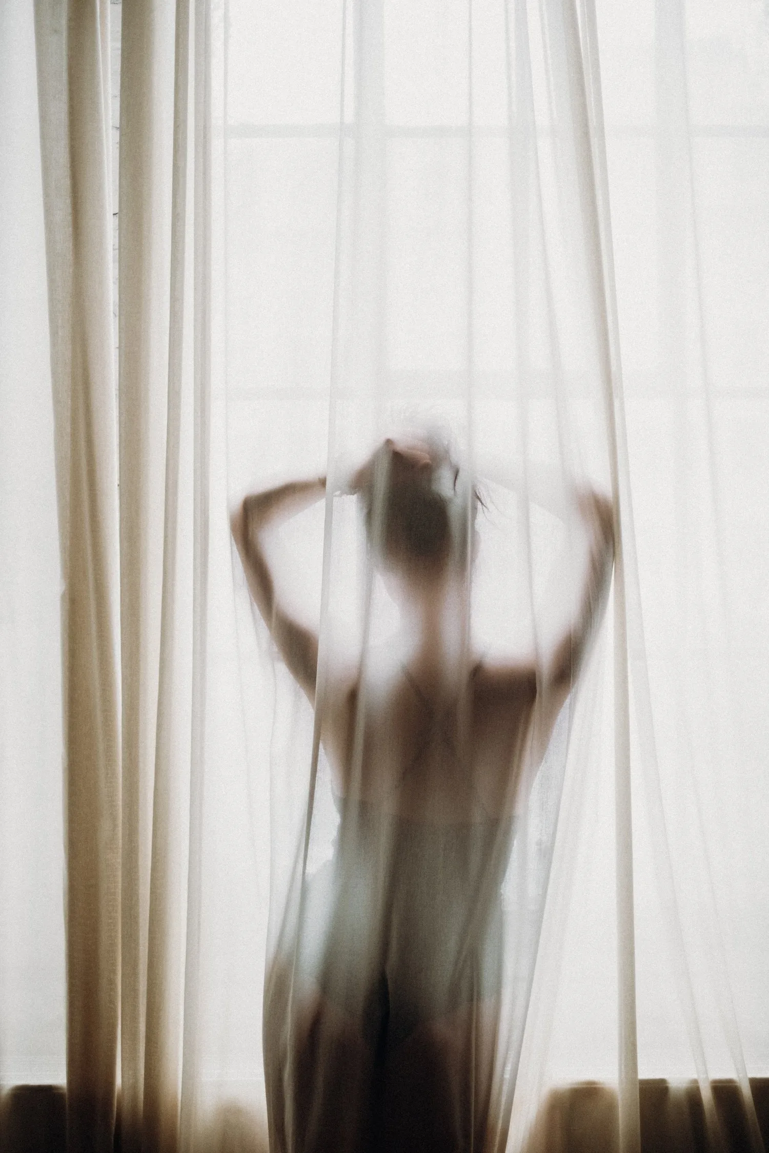 Silhouette of a person stretching behind sheer curtains