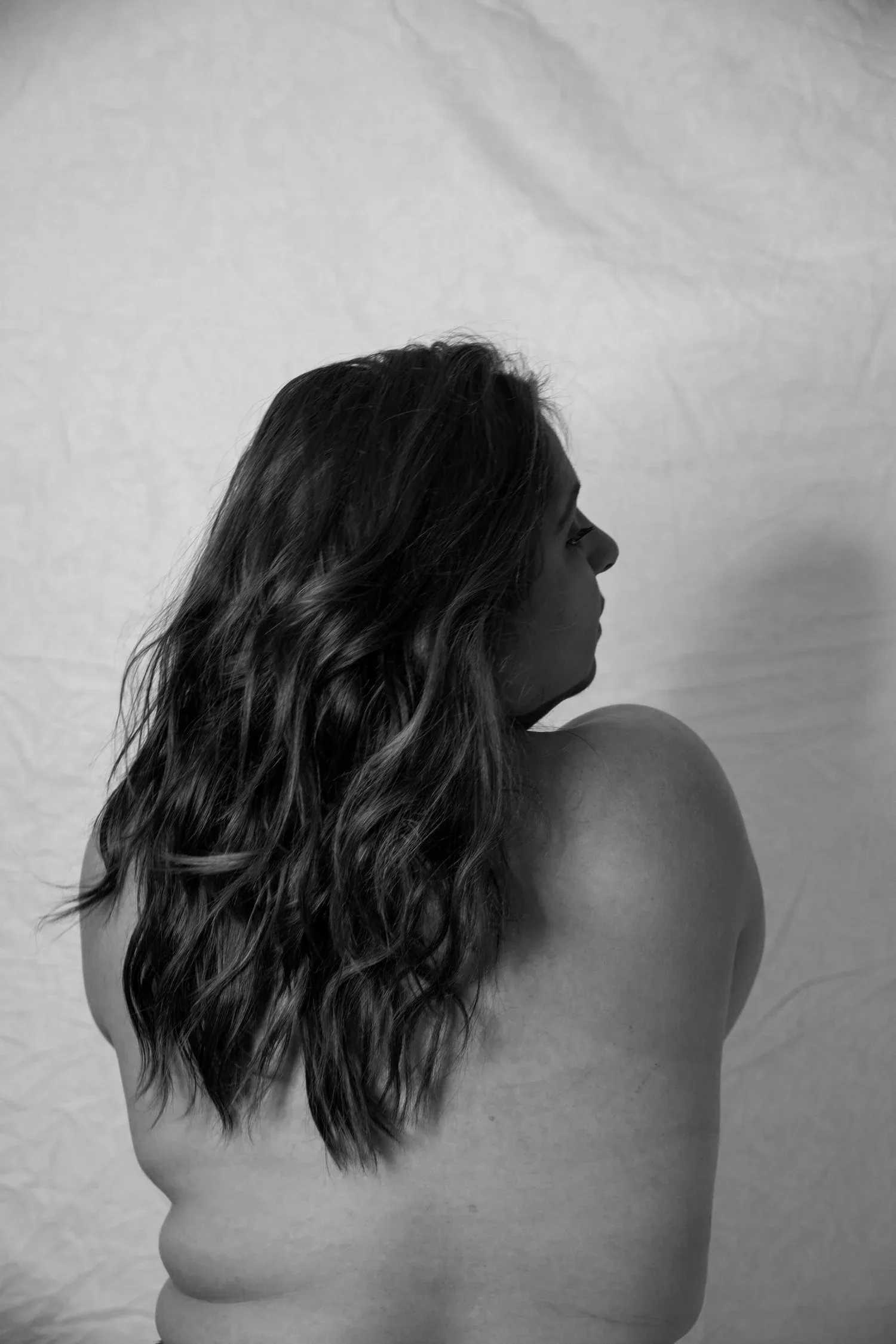 Black-and-white photo of a woman with long hair seen from behind, bare-shouldered