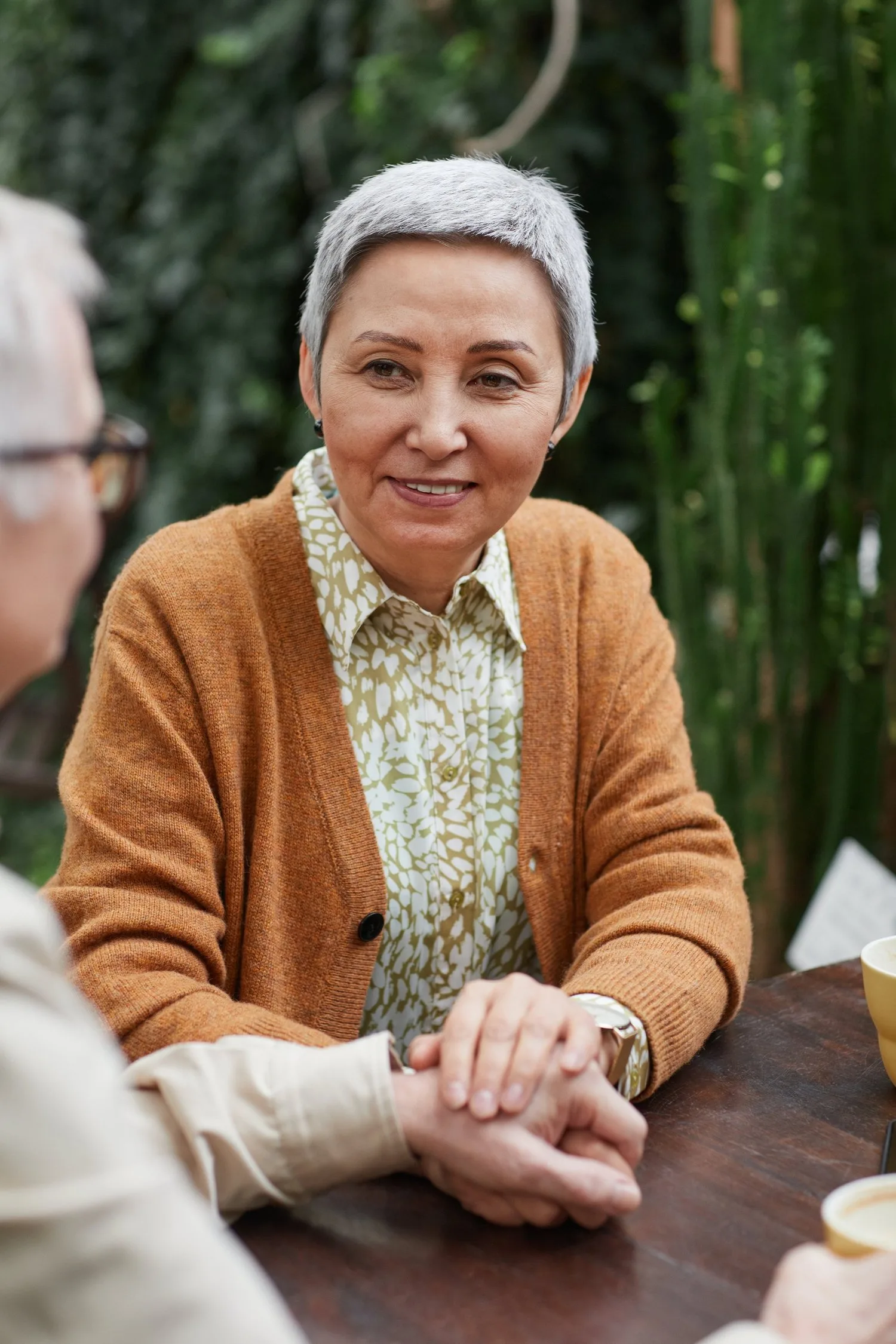 Smiling older woman in an orange cardigan seated with hands folded