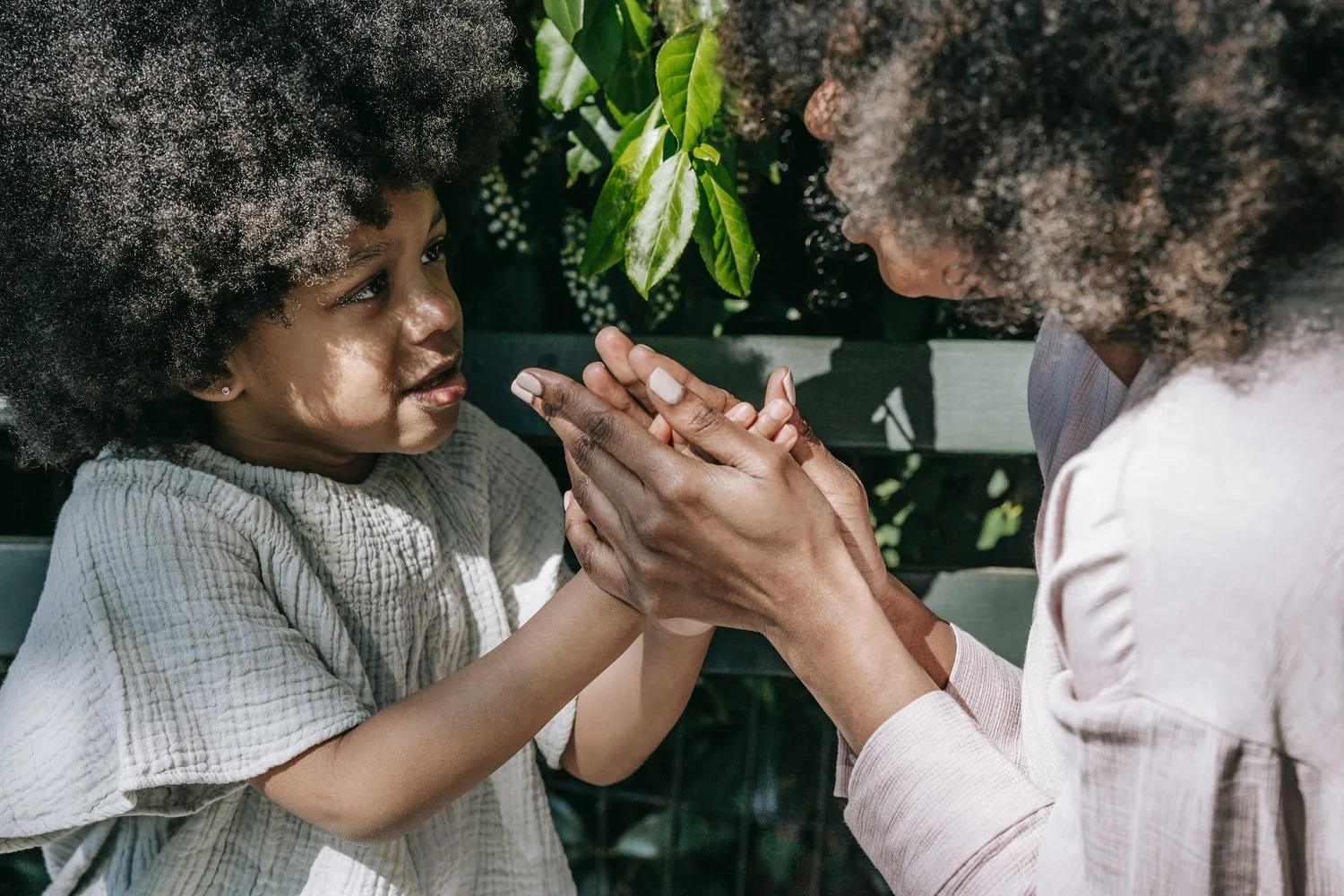 Child and adult with curly hair clapping hands together playfully