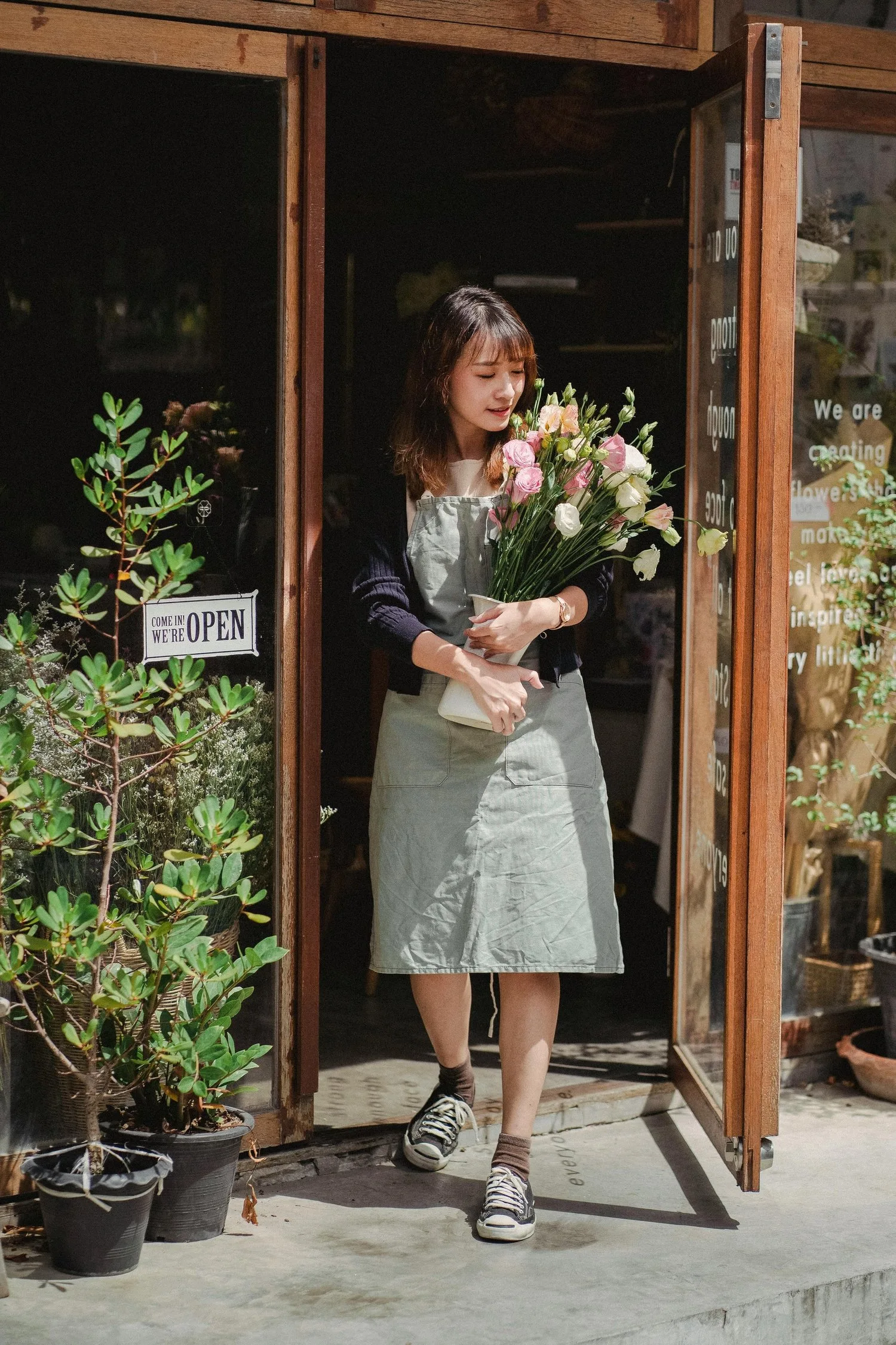 Woman holding a bouquet of flowers in the doorway of a plant-filled shop