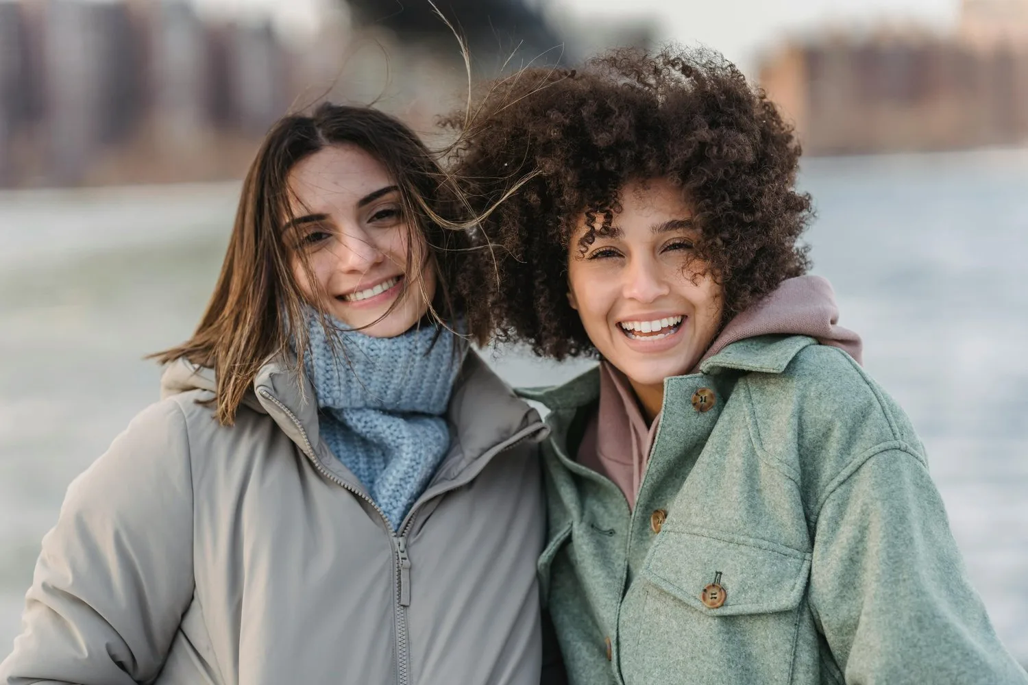 Two smiling friends in winter jackets standing close together outdoors