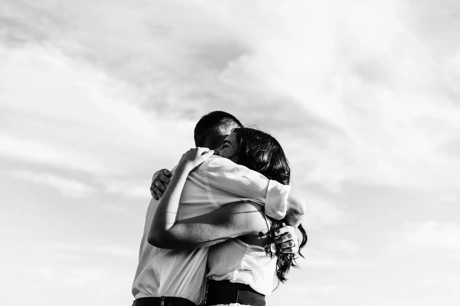 Black-and-white photo of two people embracing outdoors under a cloudy sky
