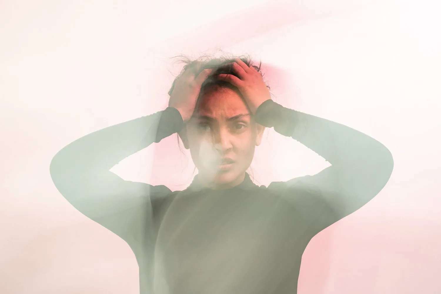 Person holding their head in both hands against a soft, blurred background
