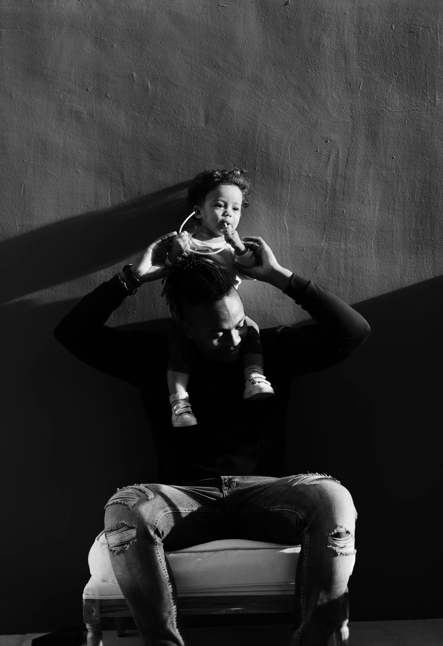 Black-and-white photo of a parent holding a toddler overhead while seated