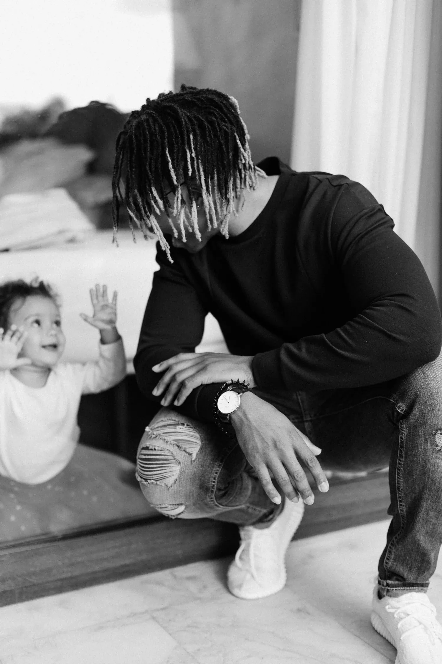Black-and-white photo of a tired father sitting on a sofa beside his baby