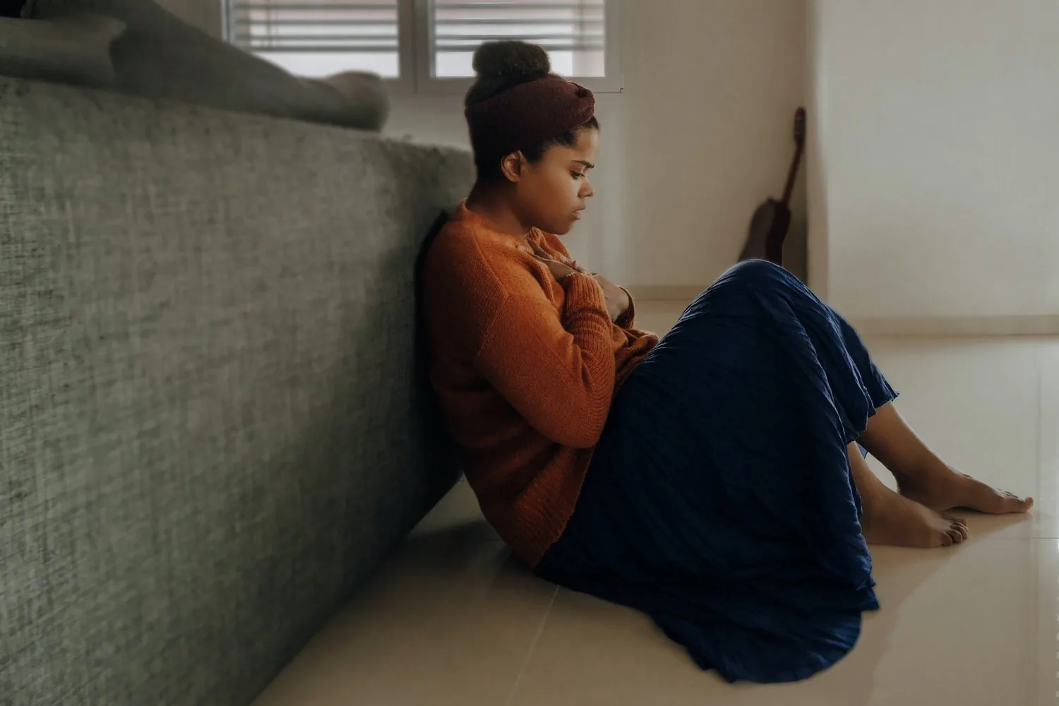 Woman sitting on the floor against a wall, looking down at her phone