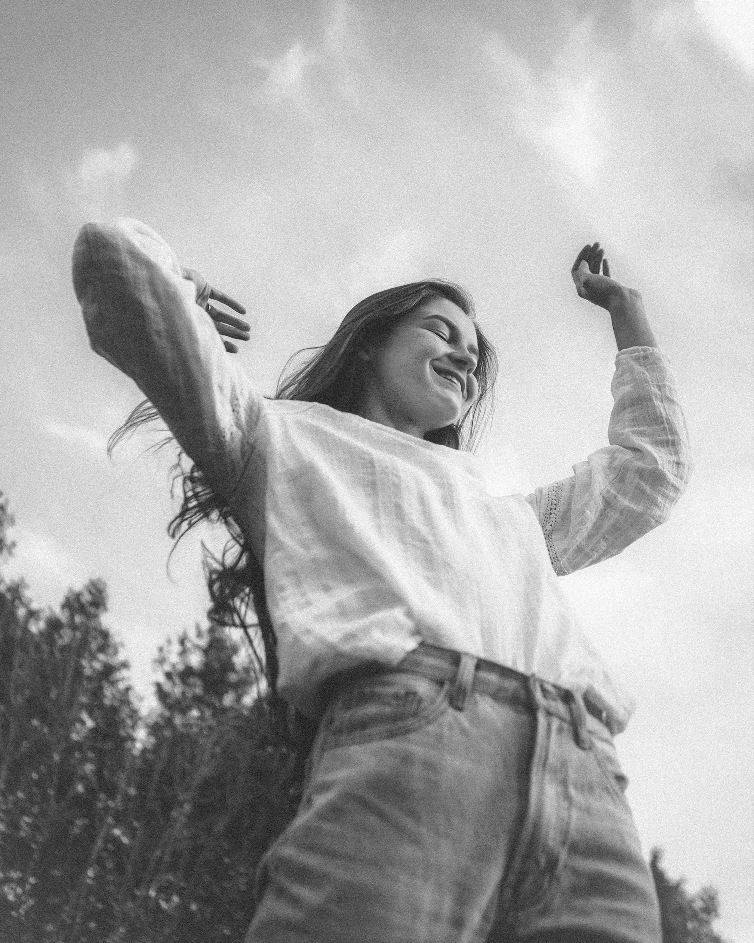 Black-and-white photo of a woman dancing joyfully outdoors with arms raised