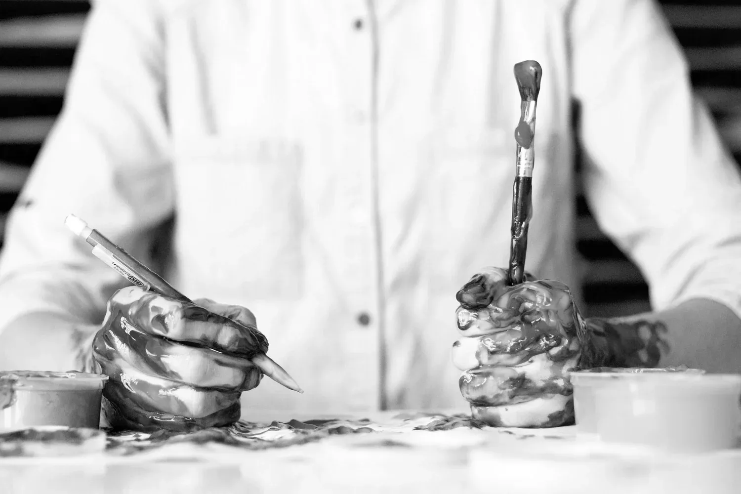 Black-and-white photo of a person in a white coat working at a cluttered counter