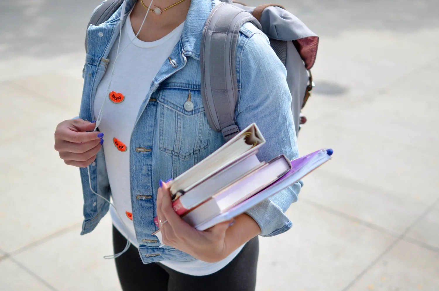 Student in a denim jacket carrying books and a backpack