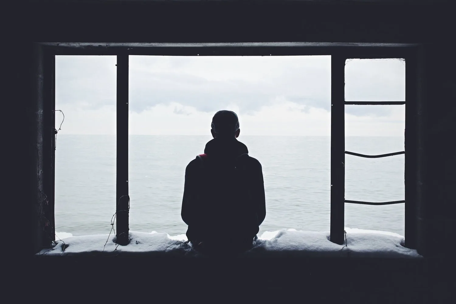Silhouette of a person seated at a large window looking out at the water