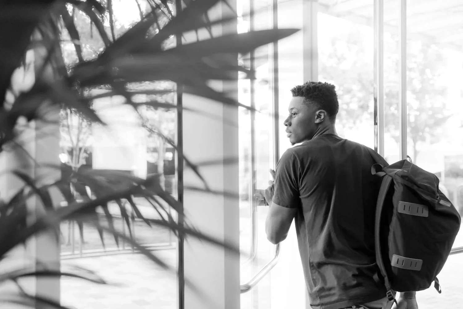 Black-and-white photo of a young man with a backpack standing in a hallway