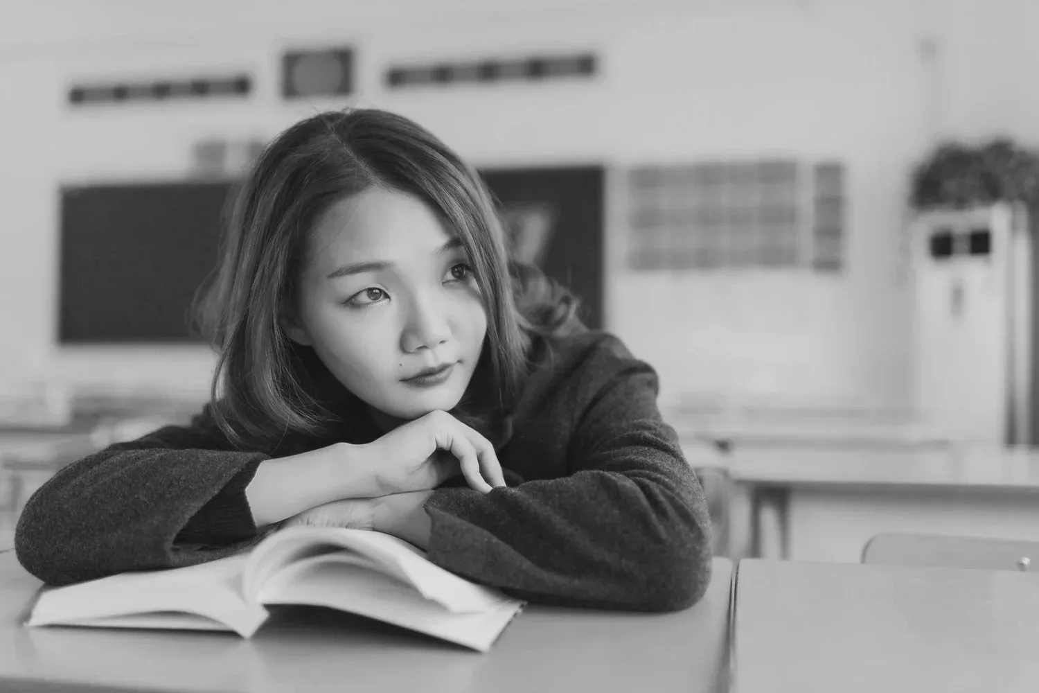 Black-and-white photo of a young woman resting her chin on an open book