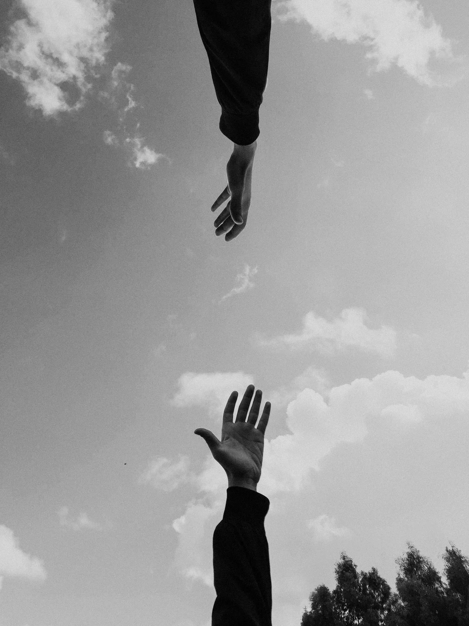 Black-and-white photo of two hands reaching toward each other against the sky
