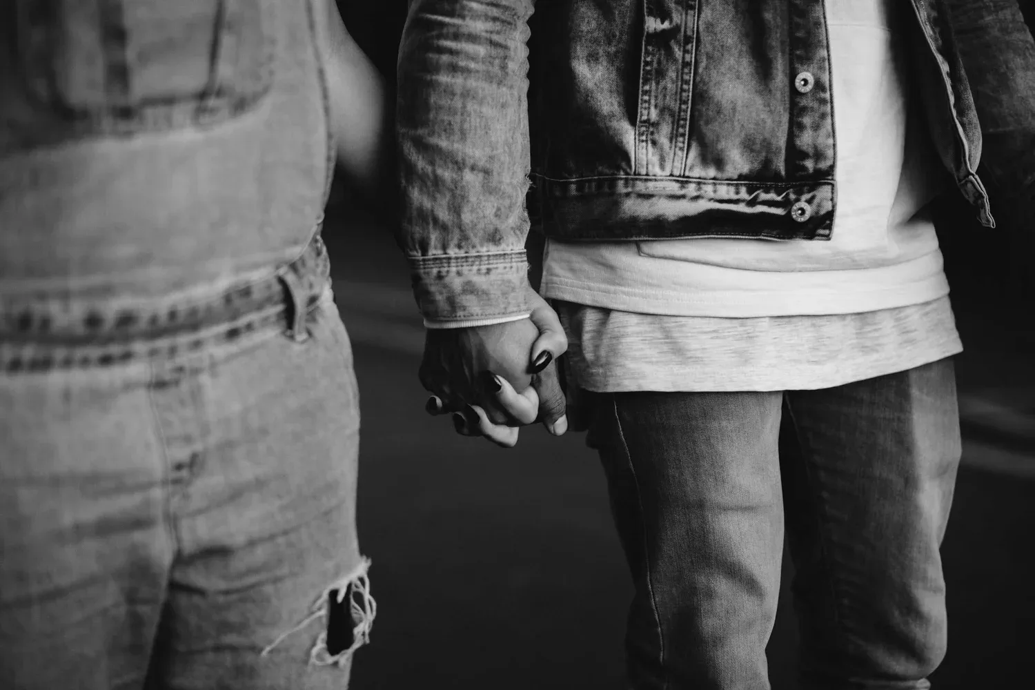 Black-and-white photo of two people holding hands, shown from the waist down